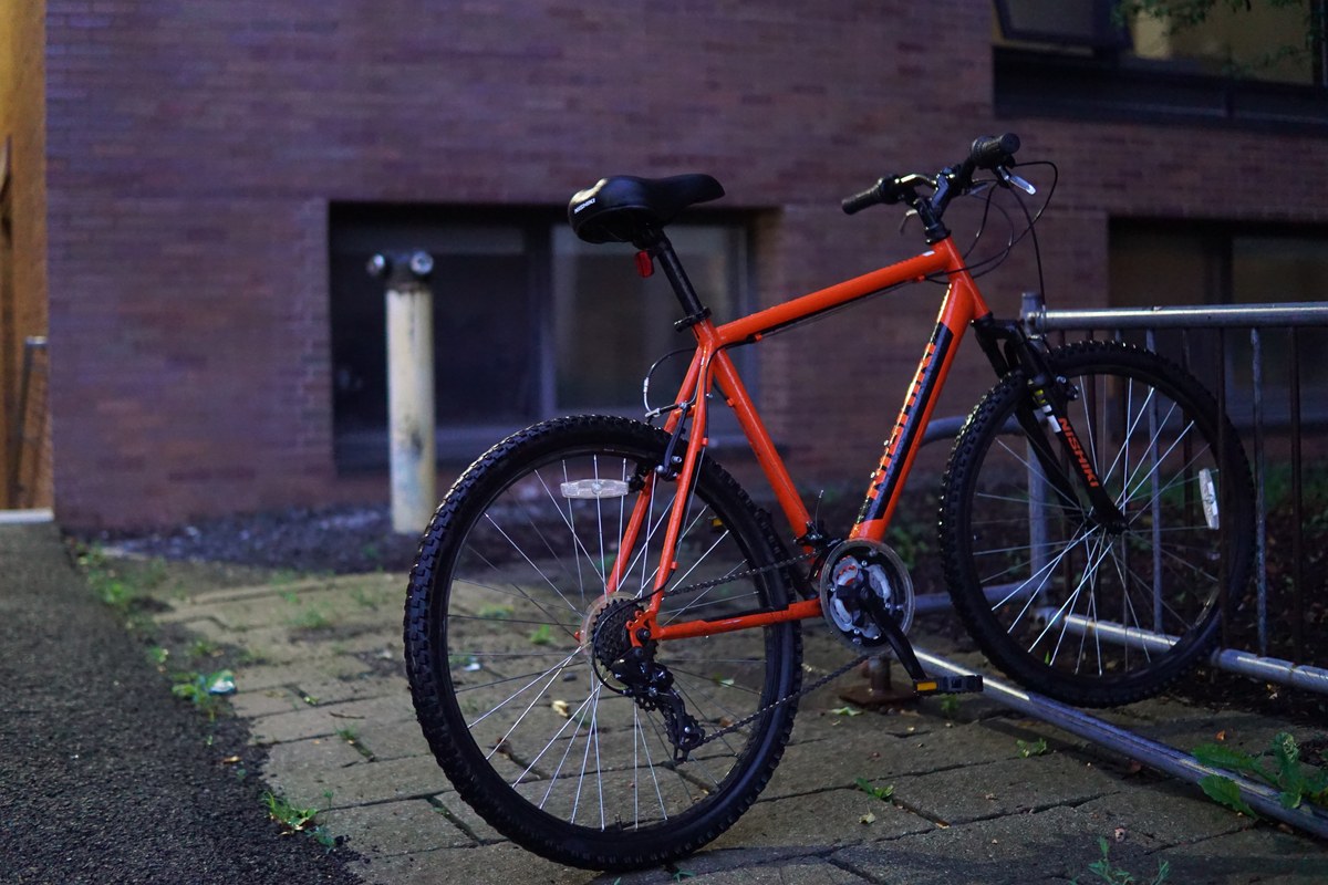 Orange bicycle locked against a brick wall